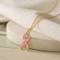 Gros plan du pendentif ruban rose sur chaîne dorée sur un fond beige délicat - Ruban Rose