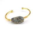 Macro shot of gold wire-wrapped gray natural crystal stone on a minimalist open bangle - Flash Stone (Labradorite)