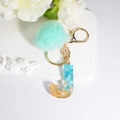 Letter J resin keychain with blue stones, gold foil, and a mint green fur pompom charm - Letter J