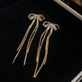 Detail van gouden strikoorbellen met zirkonia en lange vloeiende kwastjeskettingen - Strik Kwastje Stijl (Echt Verguld) / Goud