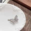 Close-up of a silver butterfly clip with sparkling rhinestones on a ceramic plate - Single Butterfly / White