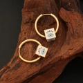 Boucles d'oreilles créoles dorées avec pendentifs cube mauvais œil sur fond de bois - Blanc