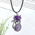 Silver cat necklace pendant with purple crystals on a black cord over book pages - Amethyst