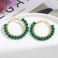Detail of handmade gold wire-wrapped hoop earrings with malachite beads on a white tray - Cyan Black Veins