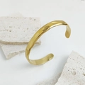 Detailansicht des goldenen offenen Armreifs mit Hammerschlag-Textur auf Travertin-Stein - 14K Vergoldeter 304 Edelstahl / Gold