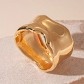 Nahaufnahme eines goldenen, unregelmäßigen Armreifs auf einer Natursteinbasis - Gold