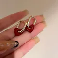 Golden oval hoop earrings featuring dark red heart drops held by hand in soft light - 18# Ear Clip - Red Heart