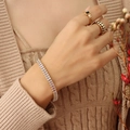 Gouden armband met heldere stenen en zwarte patroonringen aan een hand met breiwerk - Gouden Witte Zirconia Armband / 17cm
