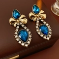 Detalle de pendientes vintage de lazo con gema azul en gota y cristales brillantes - Pendientes de gota de agua con lazo y aguja de plata - Dorado