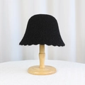 Chic black knitted bucket hat with wavy brim on wooden stand for a winter look - Black