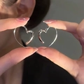 Polished silver heart-shaped hollow earrings held by hand showing minimalist design - Silver Hollow Heart Ear Cuff (A1284)