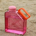 Pink transparent square sports water bottle with orange handle on a sunny beach - Red
