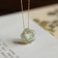 Vue détaillée du collier pendentif fleur en jade vert sur fond de livre - Jade Clair