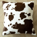 Flauschiges Kissen mit braun-weißem Kuhmuster auf hellem Holzfußboden platziert - 45x45 cm / Milchfleece