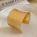 Detail view of a wide gold cuff bracelet with intricate woven texture on a white plate - Bright Gold Woven Texture Wide Cuff Style