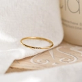 Detail of a minimalist gold zircon ring on a textured wooden tray with natural lighting - US 5 / Triple Stone / Gold