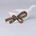 Broche nœud vintage dorée avec cristaux multicolores sur un fond blanc épuré - Or vintage avec strass multicolores