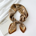 Silk square scarf with gold paisley pattern displayed on a white textured fabric - Paisley Small Border Caramel