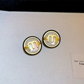 Close-up of circular earrings with m logo, shell inlay and black beaded edges - Gold Letter