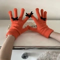 Close-up of orange knitted gloves featuring black bow accents and touchscreen finger tips - One Size / Orange