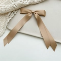 Detailed close-up of champagne gold satin bow hair clip with long elegant ribbons - Khaki