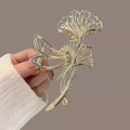 Pince à cheveux élégante en métal feuille de ginkgo dorée tenue à la main sur fond violet - Feuille de Ginkgo Évidée