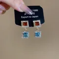 Detail of square crystal drop earrings with orange and blue stones in gold finish - Amber Orange and Sea Blue (Gold Base)