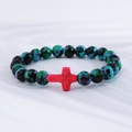 Detail of turquoise style beads with a red cross pendant on white textured fabric - Cyan Blue Black Spotted Red Cross Bracelet