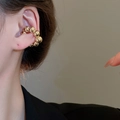 Vista macro dettagliata di un ear cuff a sfere dorate lucide sull'orecchio - Orecchini a clip (1 paio) / Oro