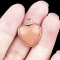 Pink quartz heart pendant with gold plated edges shown held on a finger - Pink Aventurine Gold Edging