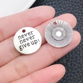 Nahaufnahme kleiner silberner Motivanhänger mit Gravur auf den Fingerspitzen - Runder Nevernevergiveup Buchstabenanhänger (2492)