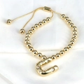 Macro shot of gold beaded bracelet featuring a cubic zirconia U-shaped charm and adjustable clasp - Letter U