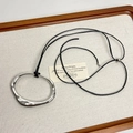 Détail du pendentif anneau argenté irrégulier sur cordon noir sur tissu blanc doux - Argenté