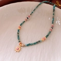 Dettaglio ravvicinato della collana di perle con ciondolo a sole su piatto in ceramica - Oro-Multicolore-Rosa