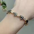 Close-up of gold chain bracelet with black enamel hearts and clear zircon stones on wrist - Black