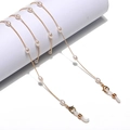 Cadena dorada para gafas con perlas y lazos de goma mostrada en un soporte blanco - Diseño de Elipse