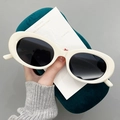 Detail of cream oval sunglasses with dark lenses next to a green velvet case - Glossy Milky White Frame Grey Lens