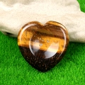 Polished tiger eye heart shaped worry stone with golden brown stripes on green grass - Tiger's Eye