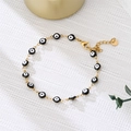 Golden Evil Eye bracelet with black and white charms on a textured background - Black Eyes Gold