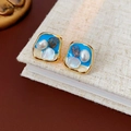 Nahaufnahme von Vintage-Viereck-Ohrringen mit blauem Emaille und Perlen auf Notizbuch - Quadratischer Blauer Perlenstil / Gold Blau Weiß