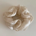 Gros plan d'un chouchou en soie blanc crème avec texture plissée et éclat satiné élégant - Beige