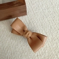 Detail of elegant tan leather bow hair clip on a soft knit fabric texture background - Light Coffee