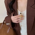 Detalle de un collar con colgante de cruz dorada vintage y cristales en un blazer - Cruz Dorada De Cuenta Ojo De Tigre / Dorado