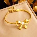 Detailed view of gold braided chain bracelet with pearl bow accent on textured display - B1431