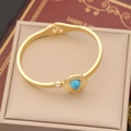 Bracelet jonc en acier doré avec pendentif turquoise et zircon sur un coussin à bijoux - Bracelet