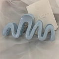 Detail of light blue wave-shaped claw clip showing smooth material and spring mechanism - Blue