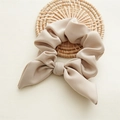 Detail of silk-like satin bow hair tie in beige resting on a woven rattan mat - Beige