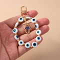 Detailaufnahme eines Hamsa-Hand- und Evil-Eye-Schlüsselanhängers mit goldenem Karabiner - Weiße Augenpalme