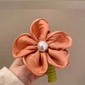 Salmon silk flower hair tie with pearl center and green spiral grip held in hand - Orange Flower Telephone Wire Hair Tie