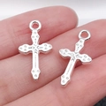 Pair of silver-tone metal cross pendants for DIY jewelry making shown on fingertips - Patterned 21x11mm (0.8g)